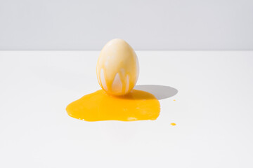 Yema de huevo líquida cayendo sobre un huevo blanco en una mesa blanca con fondo gris