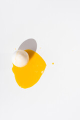 Yema de huevo líquida cayendo sobre un huevo blanco en una mesa blanca. Vista superior