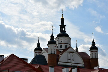 Fototapeta na wymiar A view of several domes and towers of an old Orthodox monastery with many decorative elements seen in the middle of a small Polish village on a cloudy yet warm summer day during a hike