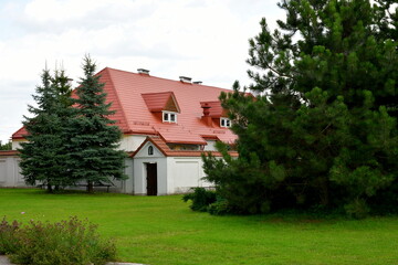 A view of the entrance to an old abandoned monastery located behind a concrete gate with a small roof located at the end of a well maintained lawn with some trees growing within its scope in Poland