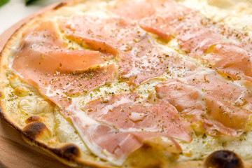 Pizza with prosciutto, cheese and oregano on wooden board close up