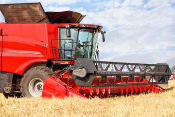 Fragment of a standing red large combine harvester for harvesting wheat on a summer day.