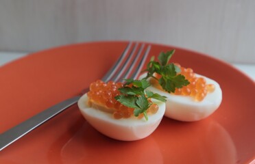Red caviar with parsley lies on boiled and cut eggs on an orange plate.