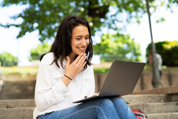 Young businesswoman sitting on steps outdoors and working on laptop. Beautiful girl learning in the park