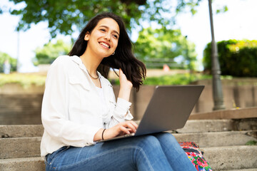 Young businesswoman sitting on steps outdoors and working on laptop. Beautiful girl learning in the park