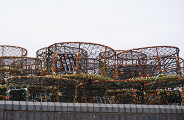 lobster pots and crab cages on wall of harbour. Stacked fishing equipment beside water in small fishing village.
