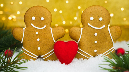 Two gingerbread men and red heart on a snowy background. Valentine's Day holiday concept. Close-up. Selective focus.
