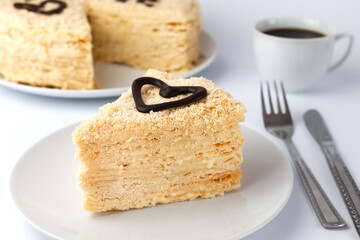 A piece of cake Napoleon on a white plate and a cup of coffee in the background. Tasty breakfast. Close-up. Selective focus.