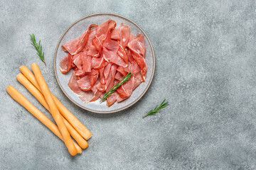 Slices of prosciutto crudo parma or jamon serrano with bread sticks. Gray grunge background. Top...