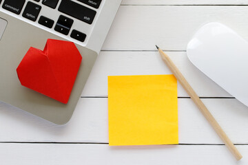 Top view of workplace decorated with Valentine's heart, blank paper note, laptop, pencil and mouse on wooden white table background