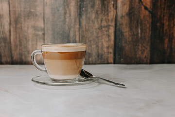 Coffee with milk in a transparent cup with an embossed spoon on a plate on a dark wooden background