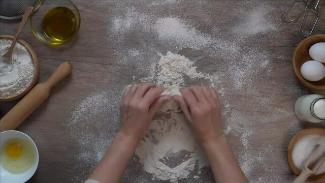Woman kneading dough on a wooden table top view