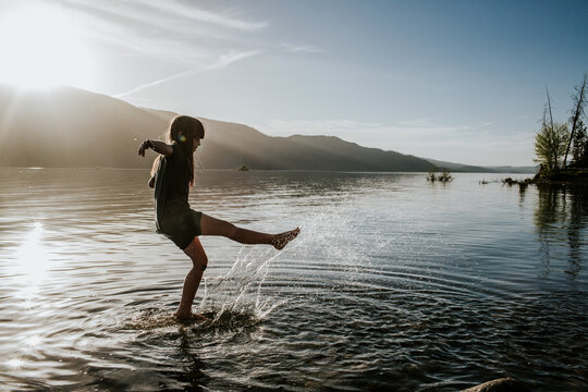 Young girl kicking and splashing in water at a lake