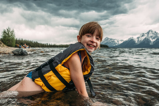 Happy young girl laying in mountain lake with life jacket