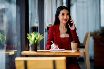 Asian Young businesswoman wearing red suit using a laptop computer. Female working on laptop in an in the cafe.