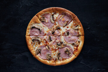 Pizza with cheese, ham, bacon and mushrooms on a black stone background. Top view