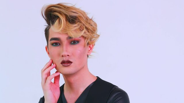 asian man with luxurious blonde hair and gorgeous make-up in white wall studio background passion look at camera