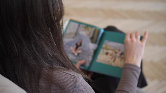 Woman sits in a chair and looks at a photo album. A person feels a memory of a past event