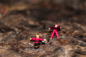A macro shot of a Guatemalan worry doll couple standing on the rocky surface of a piece of petrified wood. 