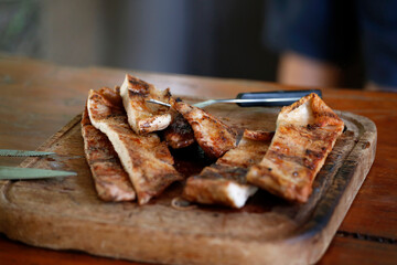 Grilled pork meat. Cooked meat. Food. Meal. Roast. Barbecue. Wooden plate with freshly cut meat slices. Argentinian barbecue. Food with proteins of animal origin. Knife and fork.