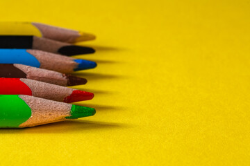 Colored pensils close up on yellow paper background. Copy space.