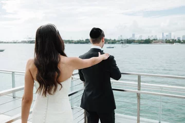 Fotobehang Bride and Groom standing in terrace outdoors Groom waits for his beloved The first meet of the brunette bride in white dress and groom in a black suit and  Kippah Jewish wedding Back view © Precious 