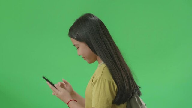 Side View Of Asian Girl Student Use Mobile Phone And Walking To School On Green Screen Chroma Key
