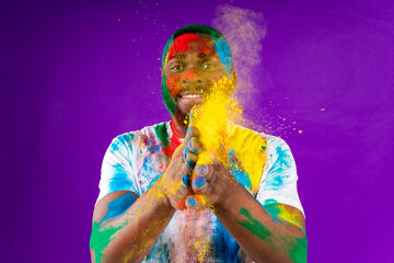Afro american man celebrate holi festival in violet studio background