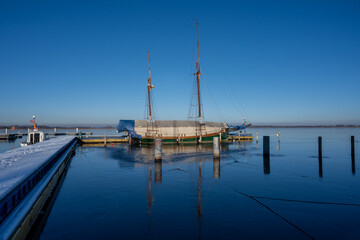 Fototapeta na wymiar A sailboat in a marina closed down for winter. Blue water and a clear blue sky