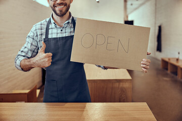 Joyful man holding open sign and giving thumbs up