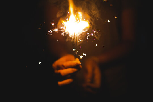 Christmas and new year eve concept image with close up of a pair of man hands taking a red fire sparkler to celebrate the night party - focus on fireworks and hope for people future