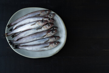 Fresh blue whiting on a plate on a black background. Copy space. Top view. Micromesistius poutassou