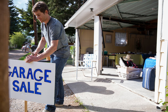 Couple Putting Up Garage Sale Sign In Yard