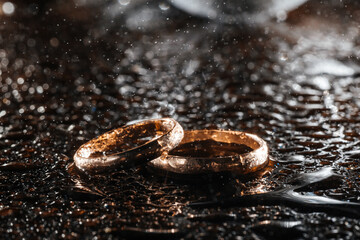Two gold wedding rings in rain drops on a black wet background