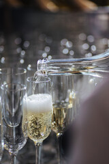 The waiter pours champagne from a bottle into a transparent glass, bubbles from a drink