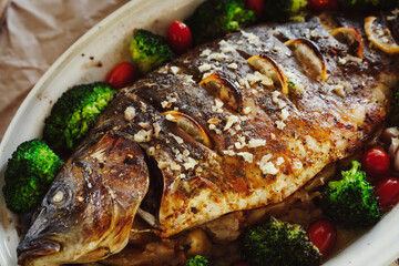 Baked fish carp with apples, broccoli, cherry tomatoes, garlic, lemon and herb spices in baking pan. Healthy eating concept.