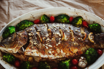 Baked fish carp with apples, broccoli, cherry tomatoes, garlic, lemon and herb spices in baking pan. Healthy eating concept.