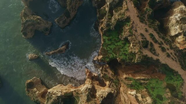Aerial shot, directly above raging ocean and Ponta da Piedade headland with group of rock formations yellow cliffs along limestone coastline, Lagos town, most famous touristic attractions of Portugal