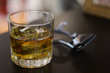 Glass with whiskey next to a razor on a wooden board