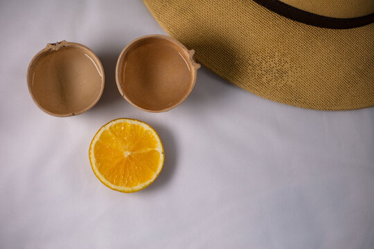 Two mezcal jicaras next to an orange red on a white background