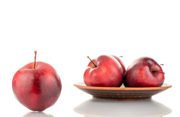 One ripe sweet, red apple in the foreground and three apples on a plate in the background, close-up, isolated on white.