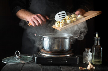 Chef cooks dumplings in a saucepan in the restaurant kitchen. Close-up of the hands of cook during work