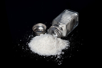 Heap of salt from a salt shaker on a black background. The concept of excessive salt intake that can be the cause of diabetes or other diseases