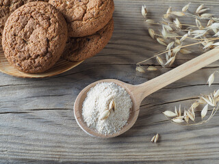 Oatmeal flour in a wooden spoon, spices, oatmeal cookies on a wooden table, flat layout, top view, closeup. Avena sativa agricultural crop powder and healthy gluten-free pastries for vegetarian