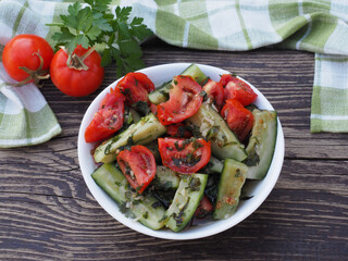 Slices of pickled cucumbers and slices of salted tomatoes with spices and herbs in a white bowl on a wooden table, flat layout. Recipe of fermented natural vegetables for dietary vegetarian food