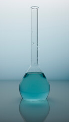 Blue liquid inside glass retort. Chemical round flask with blue water on a chemical surface. Drink pure liquid for science tests. Photo is taken with blue gradient background.