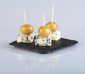 Cheese with blue mold and large green olives isolated on a white background with reflection
