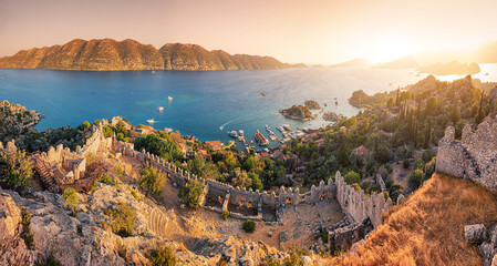 Naklejka premium Famous Simena ancient castle on a top of a hill with stunning panoramic view over the sea at sunset time. Travel and tourist attractions at Kekova island, Turkey.