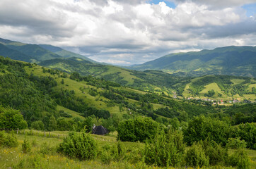 Naklejka na ściany i meble Summer mountains landscape. Hillside meadow and forest near village green grass and blue sky with clouds. Carpathians Ukraine 