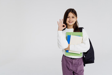 Student child girl wearing backpack hold book over isolated white background doing ok sign with fingers, excellent symbol